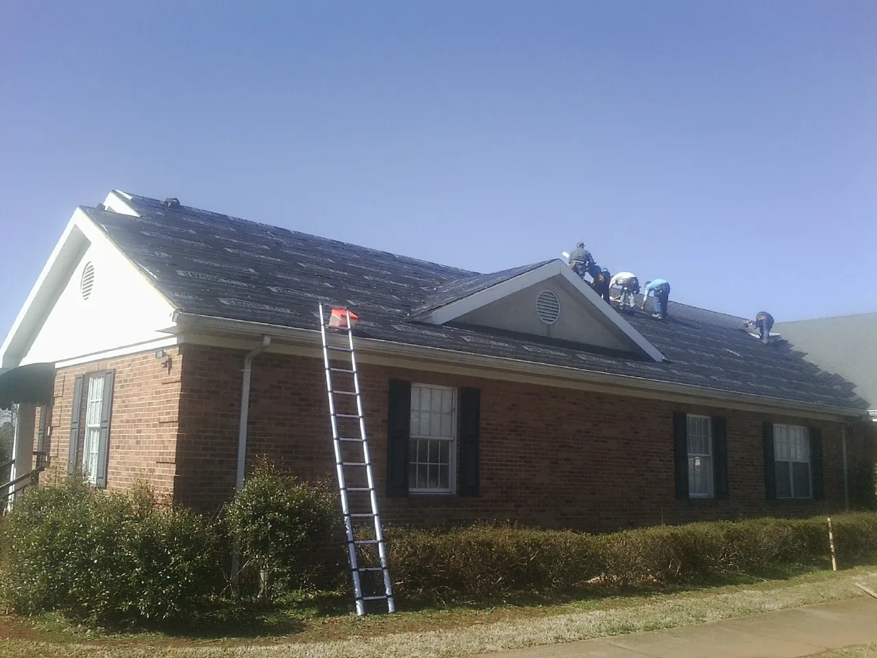 Crew tearing shingles off a brick ranch roof with a ladder set — Metal Roof Repair work by our crew in Tiro