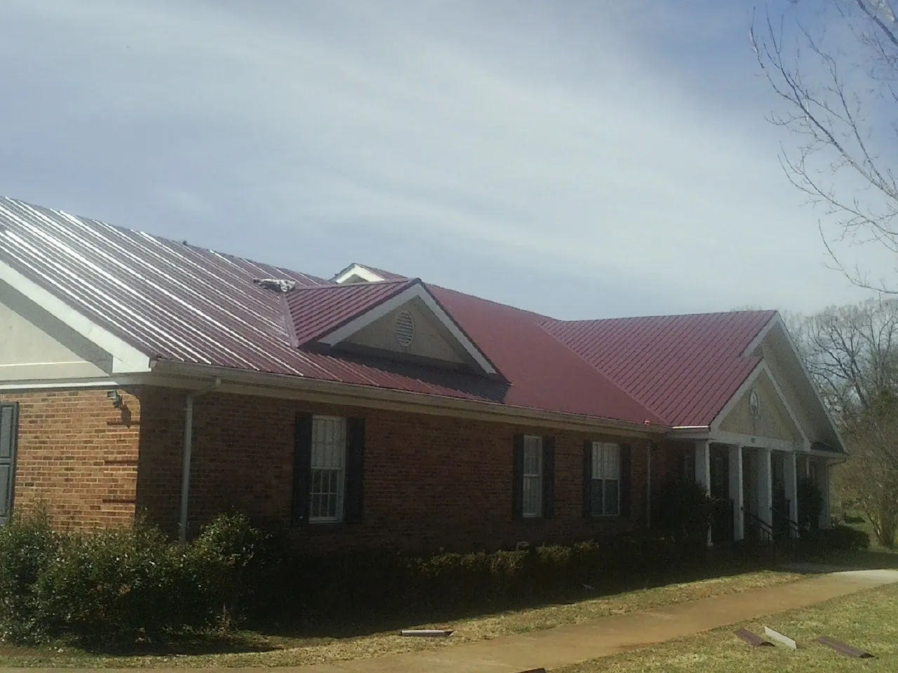 Red metal roof with gabled entries on a long brick building, from a Hail Damage Roof Repair job in Tiro