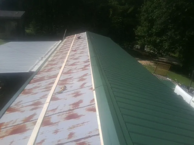Old rusted panels beside newly installed green metal roofing — Wind Damage Roof Repair by Roofing Brothers in Tiro