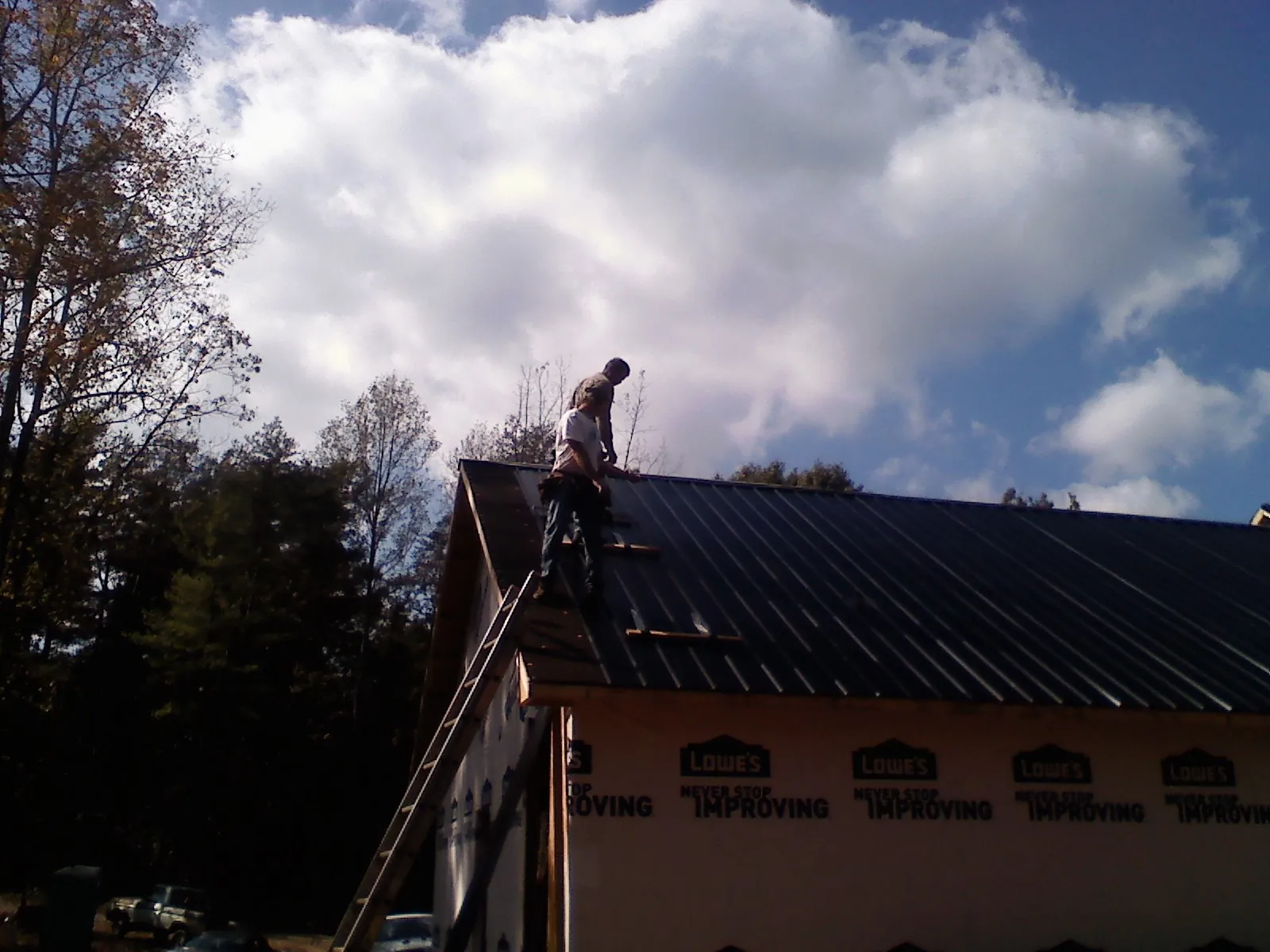 Roofer fastening dark metal panels high against a cloudy sky, from a Roof Inspection job in Tiro