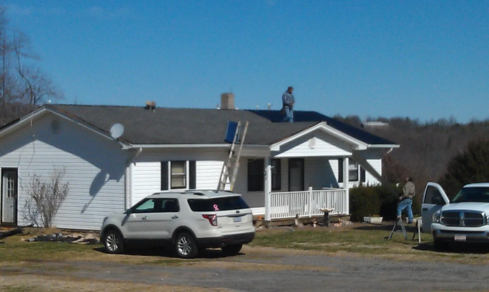 Roofers stripping shingles from a white ranch house roof in Tiro